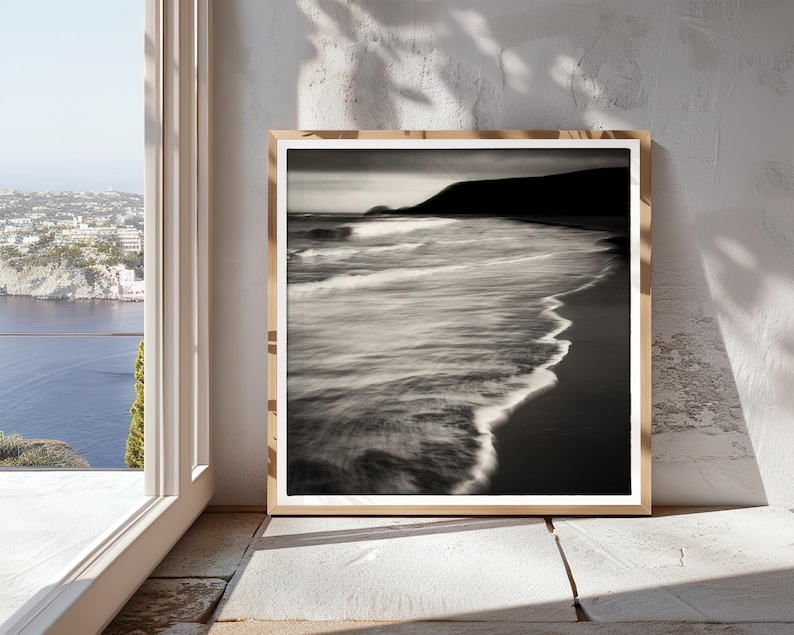 May include: A black and white photograph of a beach scene with waves crashing on the shore. The photo is framed in a light wood frame.