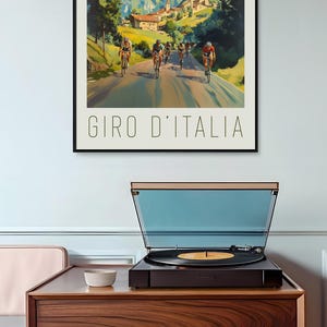 May include: A vintage poster advertising the Giro d'Italia cycling race. The poster features a group of cyclists riding through a mountain pass with a village in the background. The text "GIRO D'ITALIA" is printed at the bottom of the poster.