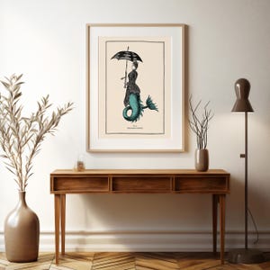 May include: A vintage illustration of a mermaid with a black and white umbrella. The mermaid is wearing a black dress and has a teal tail. The illustration is framed and hanging on a wall above a wooden console table.