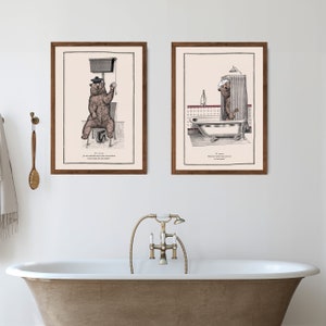 May include: Two framed illustrations of a bear in a bathroom setting. The first image shows the bear sitting on a toilet with a roll of toilet paper. The second image shows the bear standing in a bathtub with a shower curtain. Both images have text in French.