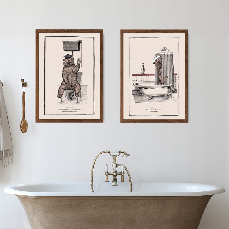 May include: Two framed illustrations of a bear in a bathroom setting. The first image shows the bear sitting on a toilet with a roll of toilet paper. The second image shows the bear standing in a bathtub with a shower curtain. Both images have text in French.