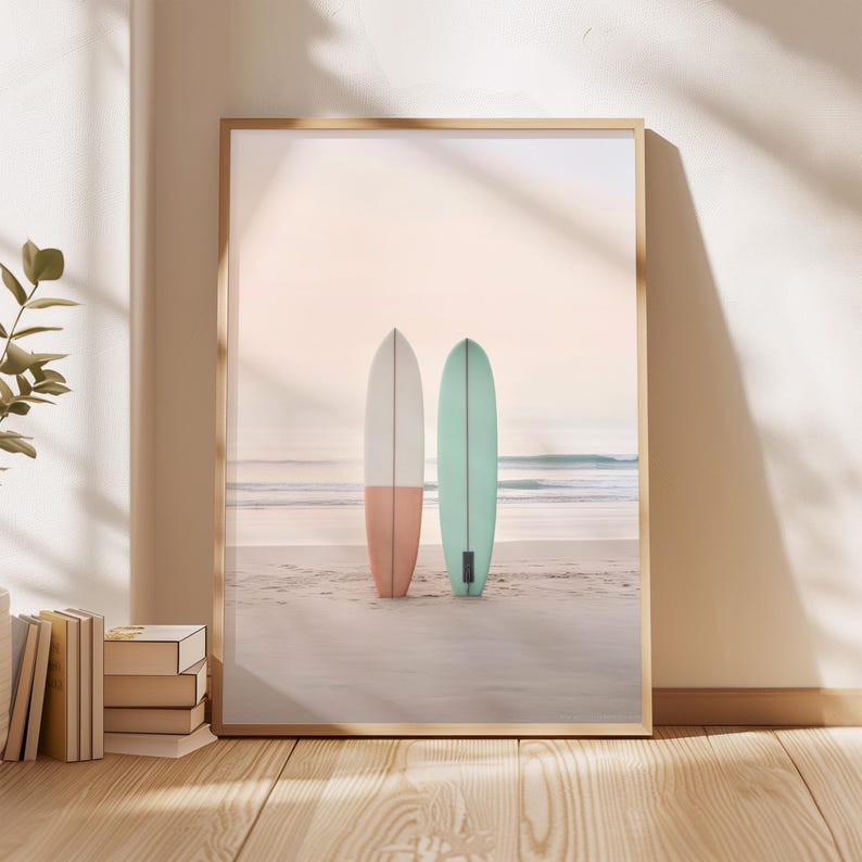 May include: Two surfboards on a sandy beach with a soft, pink and blue sky in the background. The surfboard on the left is painted pink and white, while the surfboard on the right is painted blue.