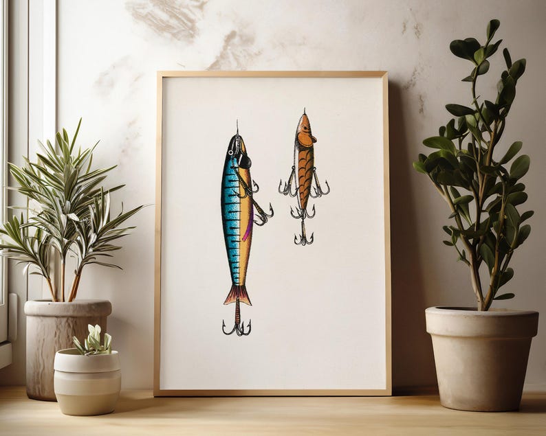 May include: A framed print featuring two detailed illustrations of fishing lures. One lure is blue, yellow, and purple, while the other is orange and brown. Both lures have multiple hooks and are set against a cream background.