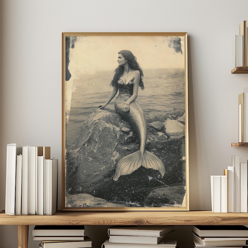 May include: A black and white vintage photograph of a mermaid sitting on a rock. The mermaid has long hair and is wearing a shell bra. Her tail is curled around the rock. The photo has a faded, antique look.