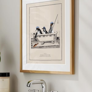 Op de afbeelding: Ingelijste kunstdruk met drie pingu&iuml;ns in een badkuip, waarvan &eacute;&eacute;n aan het vissen is. De pingu&iuml;ns dragen blauwe hoeden. Het kunstwerk is in zwart-wit met een beige achtergrond en een houten lijst. De print bevat tekst.