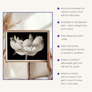 May include: A black and white floral print in a wooden frame. The image features a close-up of a flower with soft, textured petals. The frame is held by hands against a neutral background. The text on the right side says "Archival materials for vibrant colours that will last decades."