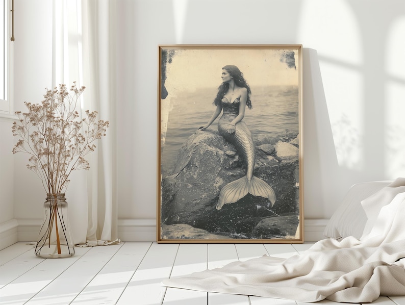 May include: A vintage-style photograph of a mermaid sitting on a rock in the ocean. The mermaid has long hair and is wearing a shell bra. The photo is in black and white and has a faded look.