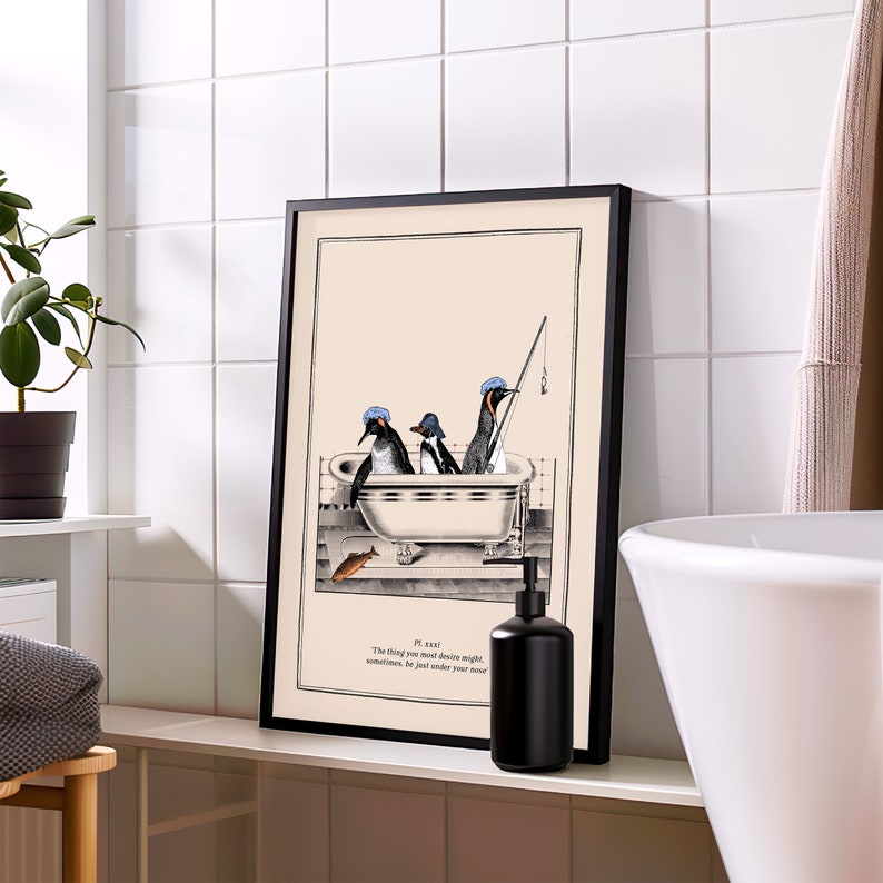 Op de afbeelding: Een ingelijste kunstdruk met drie pingu&iuml;ns in een badkuip, &eacute;&eacute;n met een hengel. Het kunstwerk is in zwart-wit met een beige achtergrond. De print bevat de tekst: "Het ding dat je het meest begeert, kan soms net onder je neus zijn."
