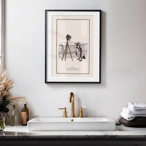 May include: Framed art print featuring a whimsical illustration of a penguin in a striped outfit and a pink hat, posing with a vintage camera on a tripod. The print includes text at the bottom.