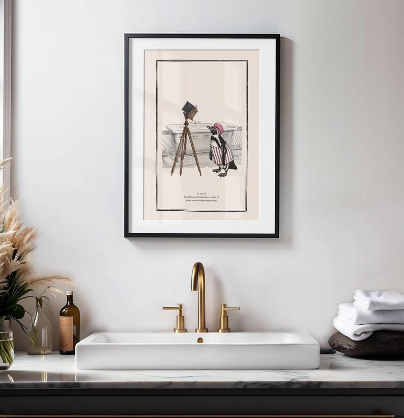 May include: Framed art print featuring a whimsical illustration of a penguin in a striped outfit and a pink hat, posing with a vintage camera on a tripod. The print includes text at the bottom.