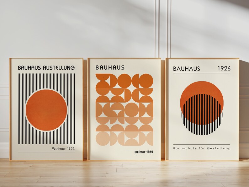 May include: Three framed prints with geometric designs in shades of orange and black. The prints feature the text "Bauhaus" and the years "1923", "1919", and "1926".