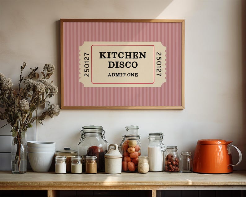 Puede incluir: Un cuadro con la inscripci&oacute;n "KITCHEN DISCO ADMIT ONE" en un dise&ntilde;o de ticket. El fondo es rosa con rayas verticales. La impresi&oacute;n est&aacute; sobre una encimera con tarros, una tetera y un jarr&oacute;n con flores.