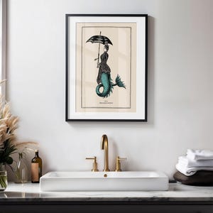 May include: A black framed print of a mermaid with a black and white umbrella. The mermaid is wearing a black dress and has a teal tail. The print is on a cream background and has the text "Pl. 18.  Hippocampus coronatus" at the bottom.