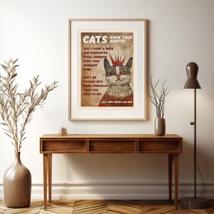May include: A vintage-style poster with a cartoon cat wearing a crown. The poster reads "Cats Know Your Rights!" and includes text about cat dominance over humans. The poster has a distressed, aged look.