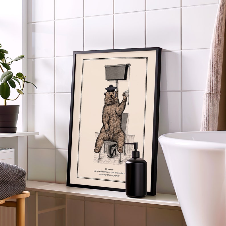 May include: A black framed print of a bear wearing a beret sitting on a toilet. The print is in a bathroom setting with a white tiled wall, a white sink, and a black soap dispenser. The text on the print reads "Je suis d&eacute;sol&eacute; mais cela n&eacute;cessitera beaucoup plus de papier."