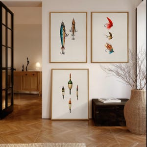 May include: Four framed art prints featuring vintage fishing lures and bobbers. The prints showcase detailed illustrations of colorful lures with hooks and bobbers in various designs. The artwork is displayed in a well-lit room with a wooden floor.