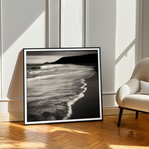 May include: Black and white photograph of a beach with waves crashing on the shore. The photo is framed in a black frame.
