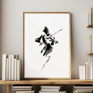 May include: Abstract black ink painting of a violinist playing a violin. The artwork is on a white background, framed in gold, and displayed on a wooden shelf with books. The painting's style is reminiscent of traditional Japanese sumi-e.