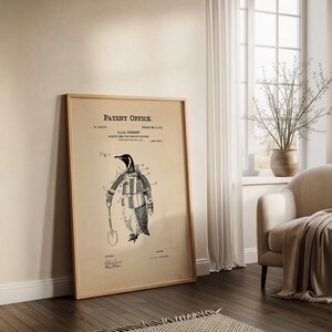 May include: A framed vintage patent print featuring a penguin in a suit holding a shovel. The print is in black and white with the words "Patent Office" at the top. The penguin is wearing a jacket and gloves. The frame is made of wood.