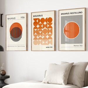 May include: Three framed prints with geometric designs in orange and black. The prints feature the text "Bauhaus" and "Bauhaus Ausstellung" with dates.