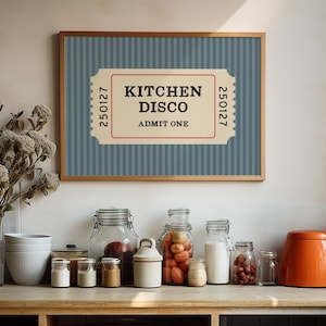 Puede incluir: Un cartel enmarcado con el texto "KITCHEN DISCO ADMIT ONE" en un dise&ntilde;o de boleto. El fondo es azul con rayas verticales. Debajo, varios frascos de vidrio y una tetera naranja se encuentran sobre una superficie de madera.