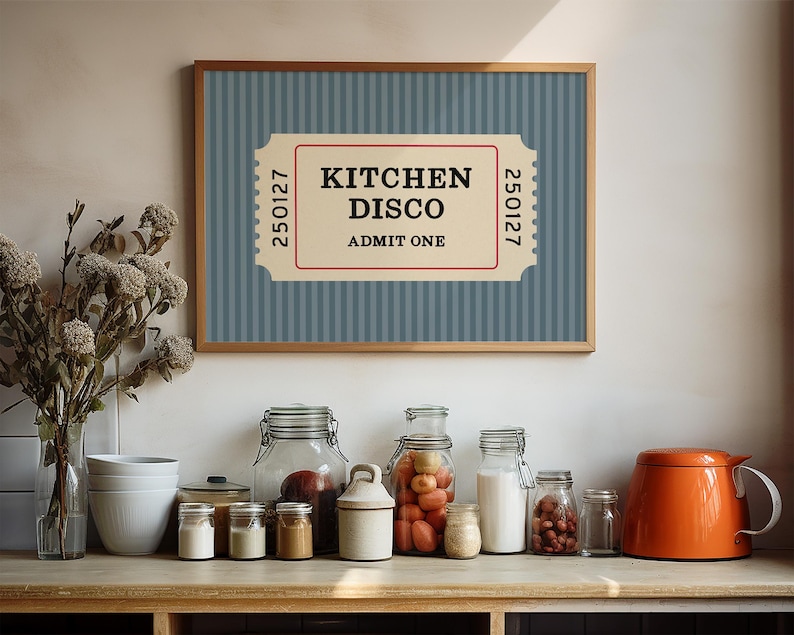 Puede incluir: Un cartel enmarcado con el texto "KITCHEN DISCO ADMIT ONE" en un dise&ntilde;o de boleto. El fondo es azul con rayas verticales. Debajo, varios frascos de vidrio y una tetera naranja se encuentran sobre una superficie de madera.