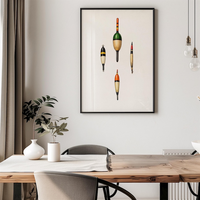 May include: A framed print featuring four vintage fishing bobbers in various shapes and colors. The bobbers are painted with orange, green, yellow, and black accents against a cream-colored background. The artwork is displayed in a black frame.