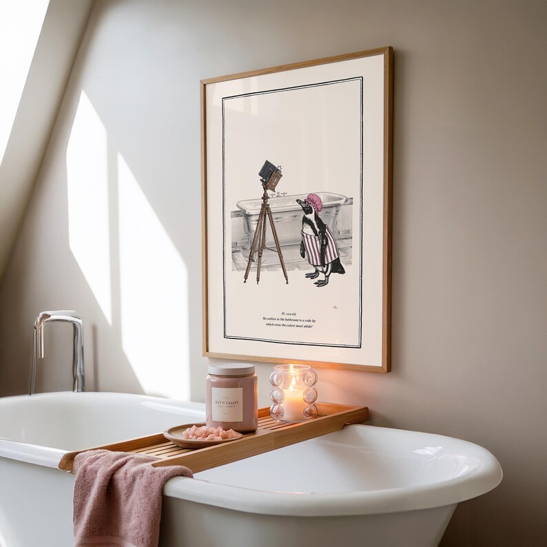 May include: A framed illustration depicts a penguin in a striped outfit and a pink hat, standing near a bathtub with a vintage camera on a tripod. A wooden tray holds a candle, a jar, and a small dish with pink contents, placed over a white bathtub.