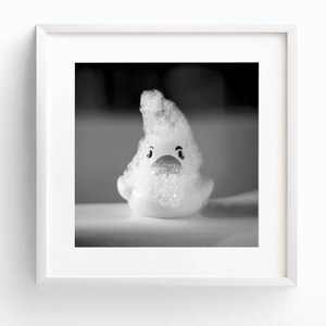 May include: A white rubber duck covered in white soap suds. The duck has black eyes and a red beak.