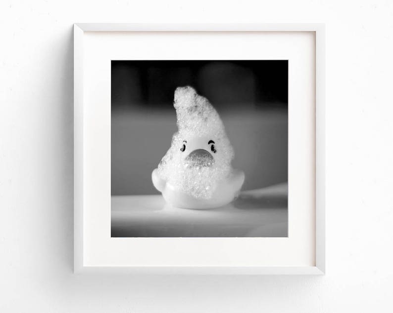 May include: A white rubber duck covered in white soap suds. The duck has black eyes and a red beak.