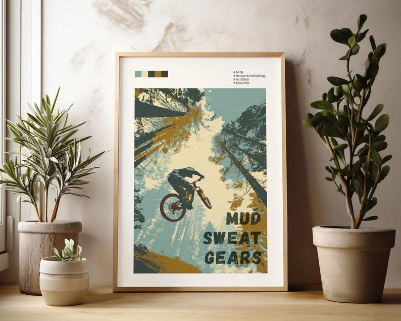 May include: A framed poster with a mountain biking theme. The artwork features a cyclist mid-air, with the text "MUD SWEAT GEARS" in bold letters. The color palette includes shades of blue, green, and brown, with a light beige background.