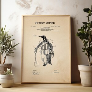 May include: A framed vintage patent print featuring a penguin in a coat and gloves holding a shovel. The print has the text "Patent Office" at the top and is displayed with potted plants on a wooden surface.