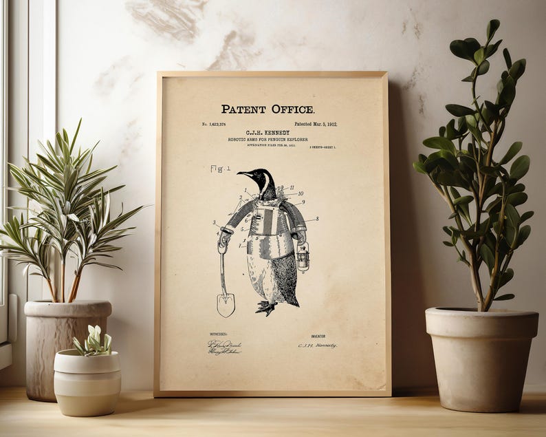 May include: A framed vintage patent print featuring a penguin in a coat and gloves holding a shovel. The print has the text "Patent Office" at the top and is displayed with potted plants on a wooden surface.