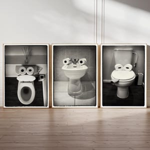 Pode incluir: Três fotografias a preto e branco emolduradas de casas de banho com rolos de papel higiénico como olhos. A primeira fotografia mostra uma casa de banho com o assento e a tampa fechados. A segunda fotografia mostra um bidé com o assento e a tampa abertos. A terceira fotografia mostra uma casa de banho com o assento e a tampa fechados.