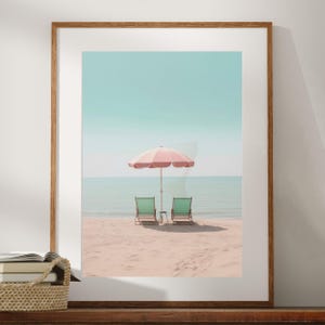 May include: Two green beach chairs sit on a sandy beach with a pink and white striped umbrella in the background.