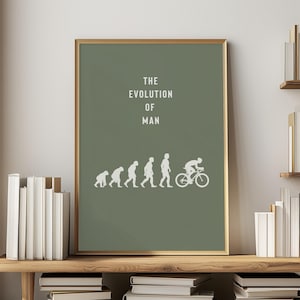 May include: A framed print with a green background and gold trim. The print features the text "THE EVOLUTION OF MAN" in white, above a series of white silhouettes depicting human evolution, culminating in a cyclist on a bicycle.