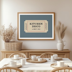 Puede incluir: Una impresi&oacute;n enmarcada con un dise&ntilde;o de boleto que dice "KITCHEN DISCO ADMIT ONE". La impresi&oacute;n tiene un fondo azul a rayas y un marco de madera. La imagen se muestra encima de una mesa de comedor con mantel y cubiertos.