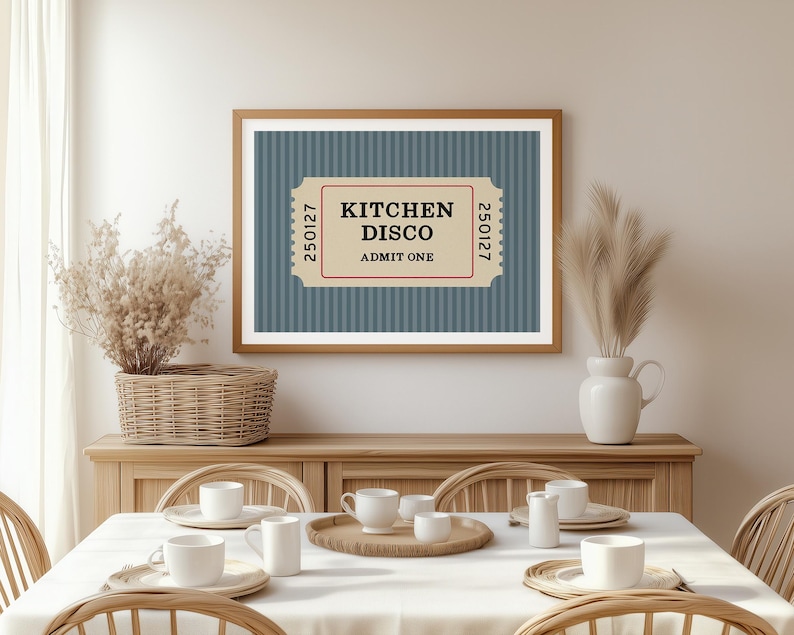 Puede incluir: Una impresi&oacute;n enmarcada con un dise&ntilde;o de boleto que dice "KITCHEN DISCO ADMIT ONE". La impresi&oacute;n tiene un fondo azul a rayas y un marco de madera. La imagen se muestra encima de una mesa de comedor con mantel y cubiertos.