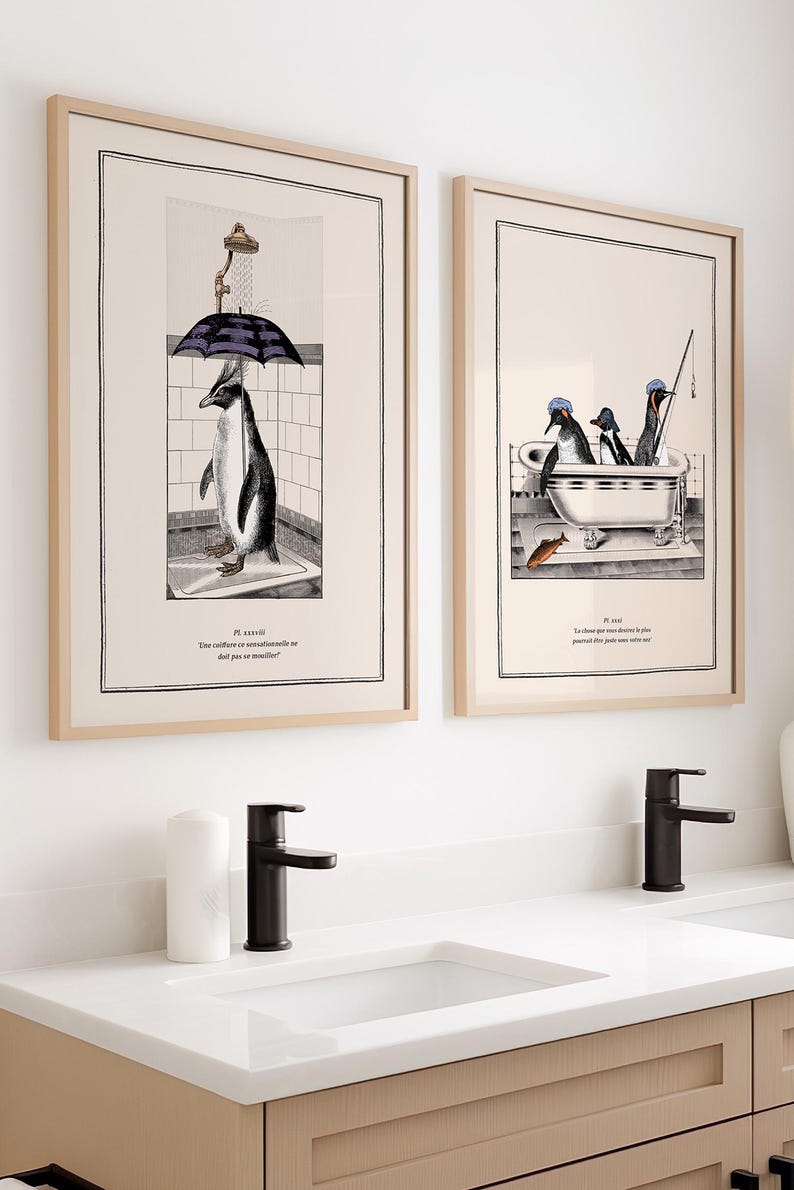 Op de afbeelding: Twee ingelijste kunstprints met pingu&iuml;nillustraties. E&eacute;n toont een pingu&iuml;n onder een paraplu in een douche, de andere toont pingu&iuml;ns in een bad. De prints hebben een beige achtergrond en zitten in licht houten frames.