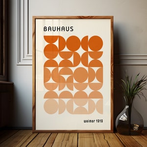 May include: A framed poster with a geometric design in shades of orange. The poster reads "Bauhaus Weimar 1919".