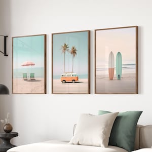 May include: Three framed prints with beach scenes. The first print shows a pink umbrella and two beach chairs on a sandy beach. The second print shows a palm tree and an orange vintage van on a sandy beach. The third print shows two surfboards on a sandy beach.