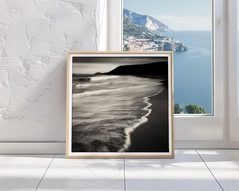 May include: A framed black and white photograph of a beach with waves crashing on the shore. The photo is in a wooden frame and is hanging on a white wall.