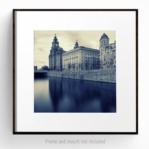 May include: A framed black and white photograph of a cityscape with buildings along a body of water. The image has a sepia tone, with the water reflecting the buildings. The frame is dark brown, and the matting is white. The text "Frame and mount not included" is at the bottom.