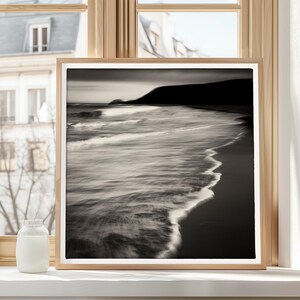 May include: A black and white photograph of a beach scene with waves crashing on the shore. The photo is framed in a simple wooden frame.