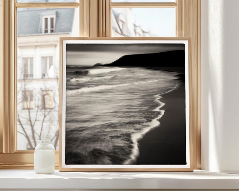 May include: A black and white photograph of a beach scene with waves crashing on the shore. The photo is framed in a simple wooden frame.