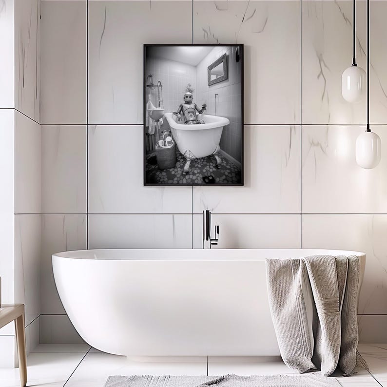 May include: A black and white photograph of a person in a bathtub. The person is wearing a hat and is sitting in a white bathtub with a shower head above it. The photo is framed and hanging on a white tiled wall.