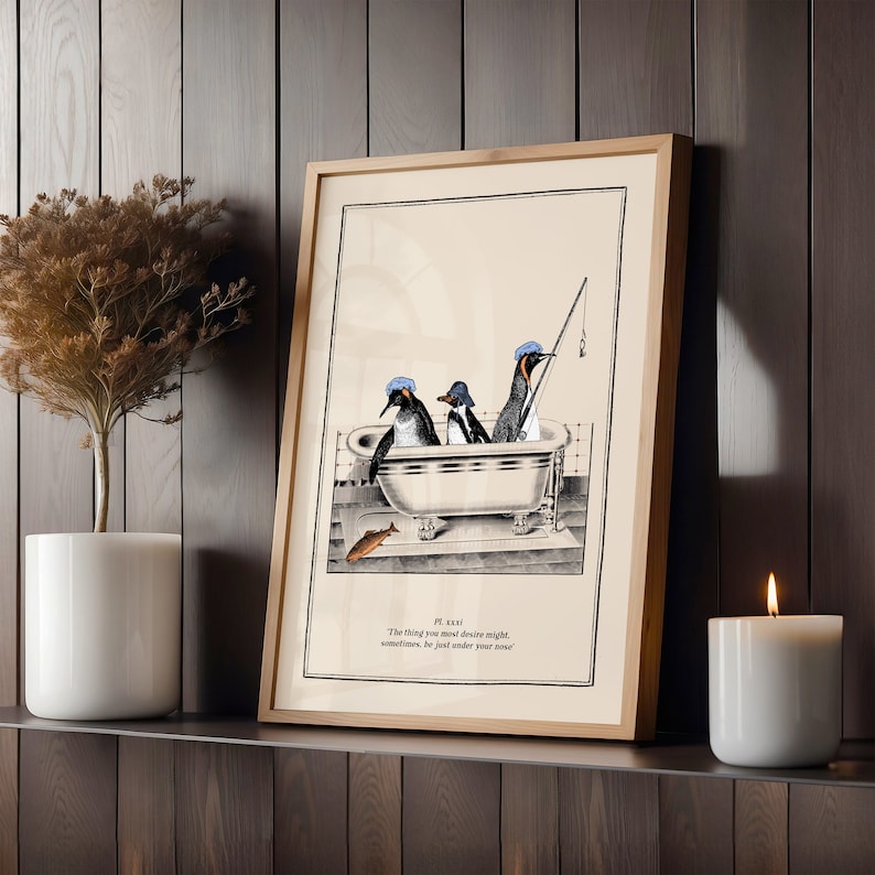 Op de afbeelding: Ingelijste kunstprint met drie pingu&iuml;ns in een badkuip, waarvan &eacute;&eacute;n aan het vissen is. De pingu&iuml;ns dragen blauwe hoeden. De print heeft een licht houten frame en bevat tekst: 'The thing you most desire might, sometimes, be just under your nose.'