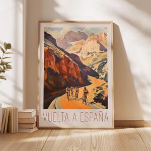 May include: A vintage poster for the Vuelta a Espa&ntilde;a cycling race. The poster features a scenic mountain road with cyclists riding through a canyon. The text "VUELTA A ESPA&Ntilde;A" is printed in red at the bottom of the poster.
