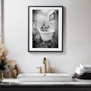 May include: A black and white photograph of a robot taking a bath in a white bathtub with four legs. The robot is wearing a white hat and has a silver body. The bathroom is tiled with white and gray tiles.