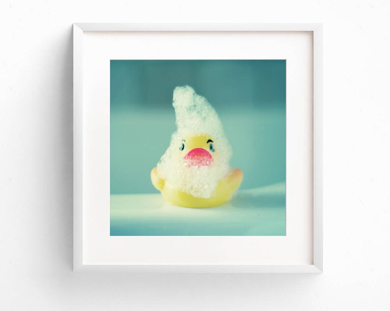 May include: A yellow rubber duck with a white foamy head and a pink beak. The duck is in a bathtub with blue water.